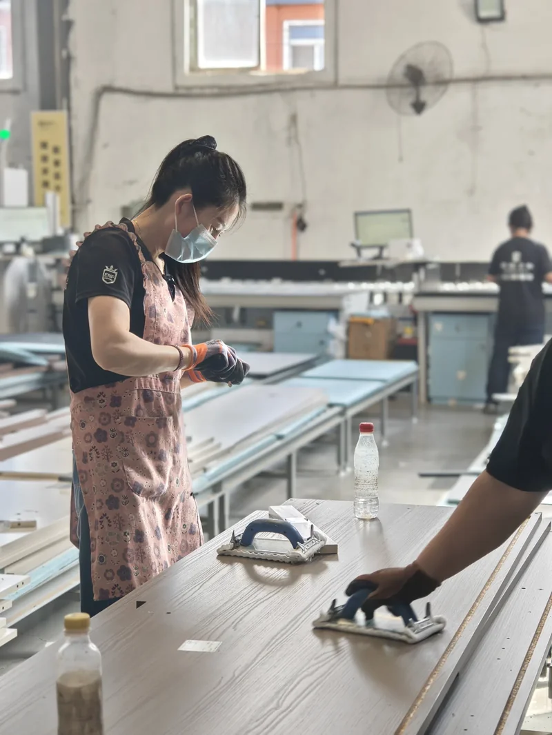 SNEJ team member checking a panel surface beside workshop equipment