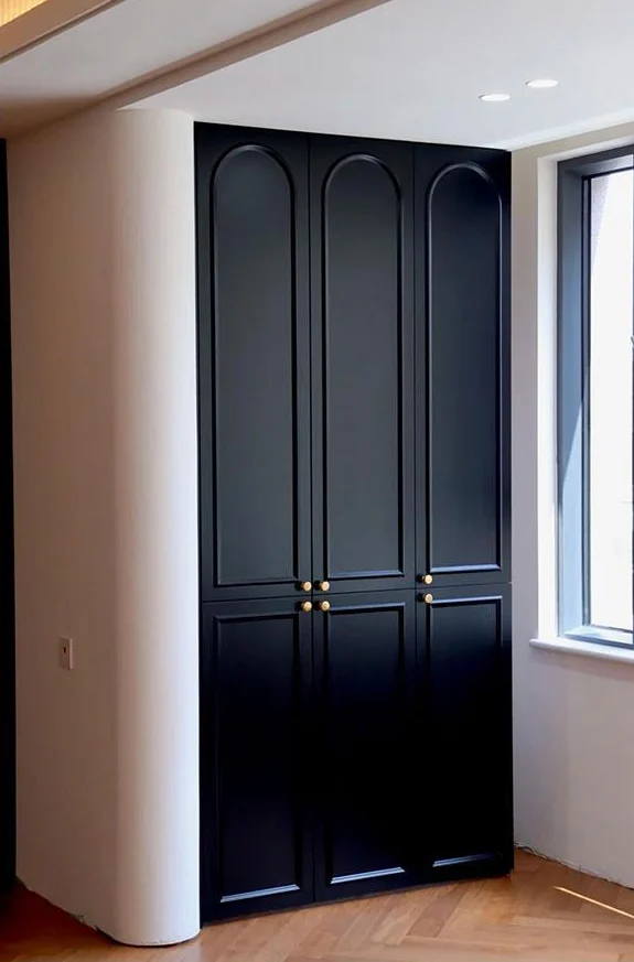 Dark floor-to-ceiling cabinet with arched panel profiles and brass-toned knobs