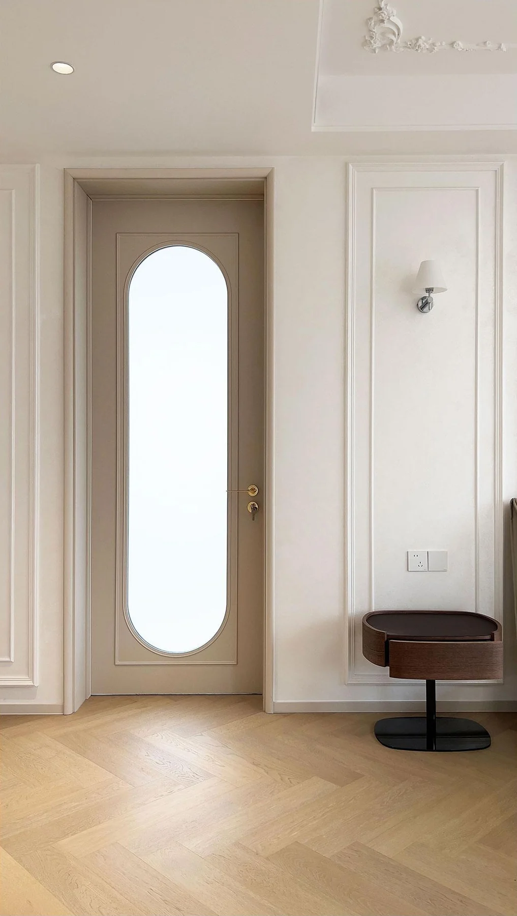 Pale interior door with a tall oval glazed inset beside decorative wall mouldings