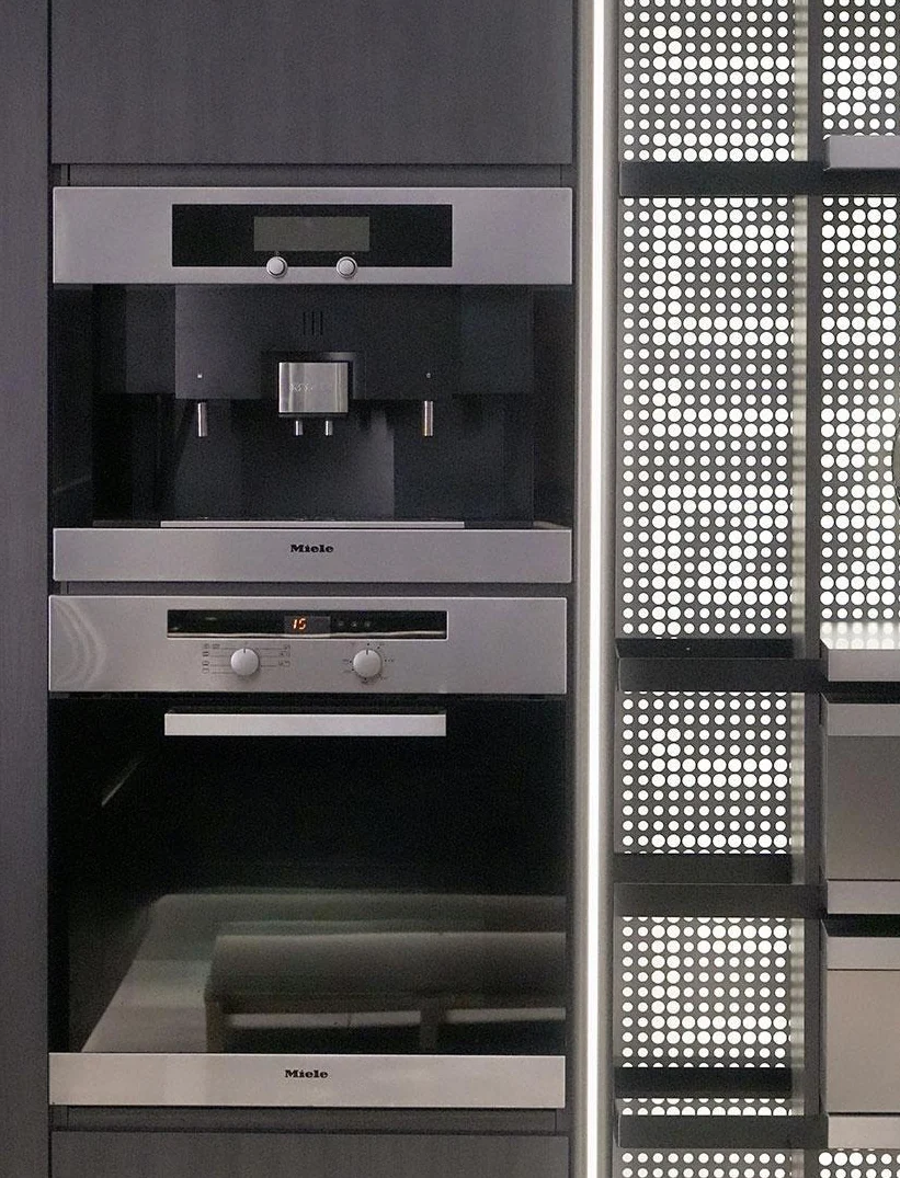 Stacked built-in appliances beside dark perforated cabinet panels