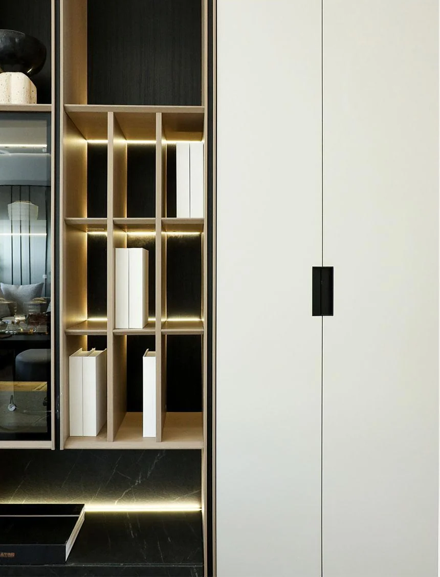 Glass-fronted display storage with illuminated shelves beside a pale cabinet door